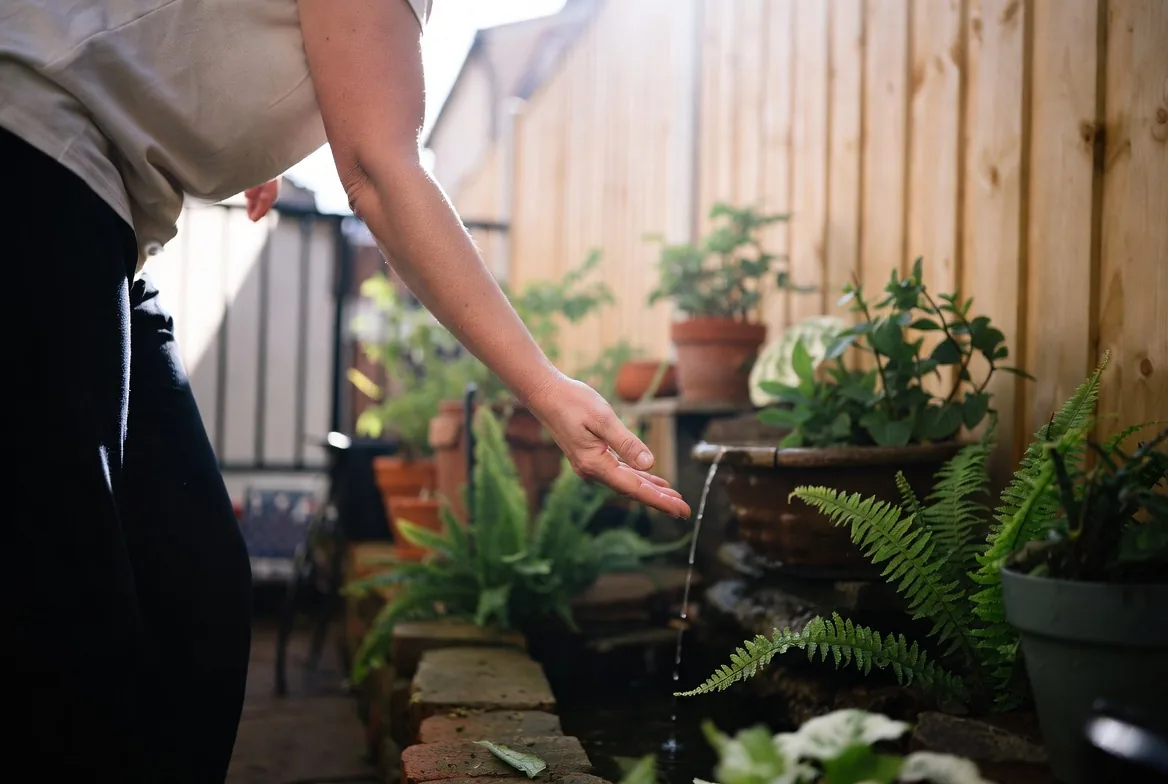 A small balcony water feature surrounded by pots and ferns